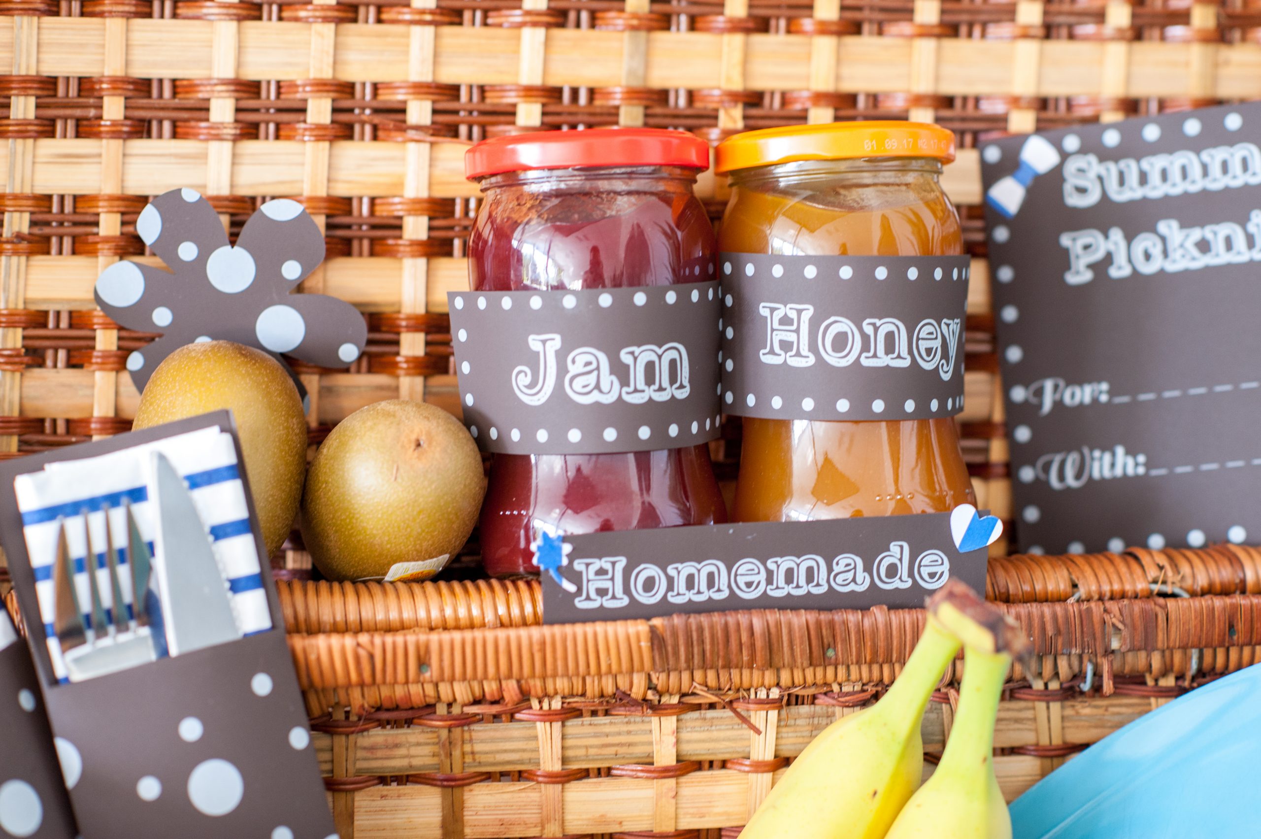 Dunkelbraune Papieretiketten mit weißem Tonerdruck an Marmeladen- und Honiggläsern im Picknickkorb, dazu Besteckhülle und Karte Summer Picknick