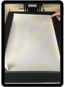 Tablet-Rahmen mit Foto: A-Folie, B-Papier und Backpapier liegen mittig in der geöffneten Transferpresse, eine Hand richtet die Lagen aus
