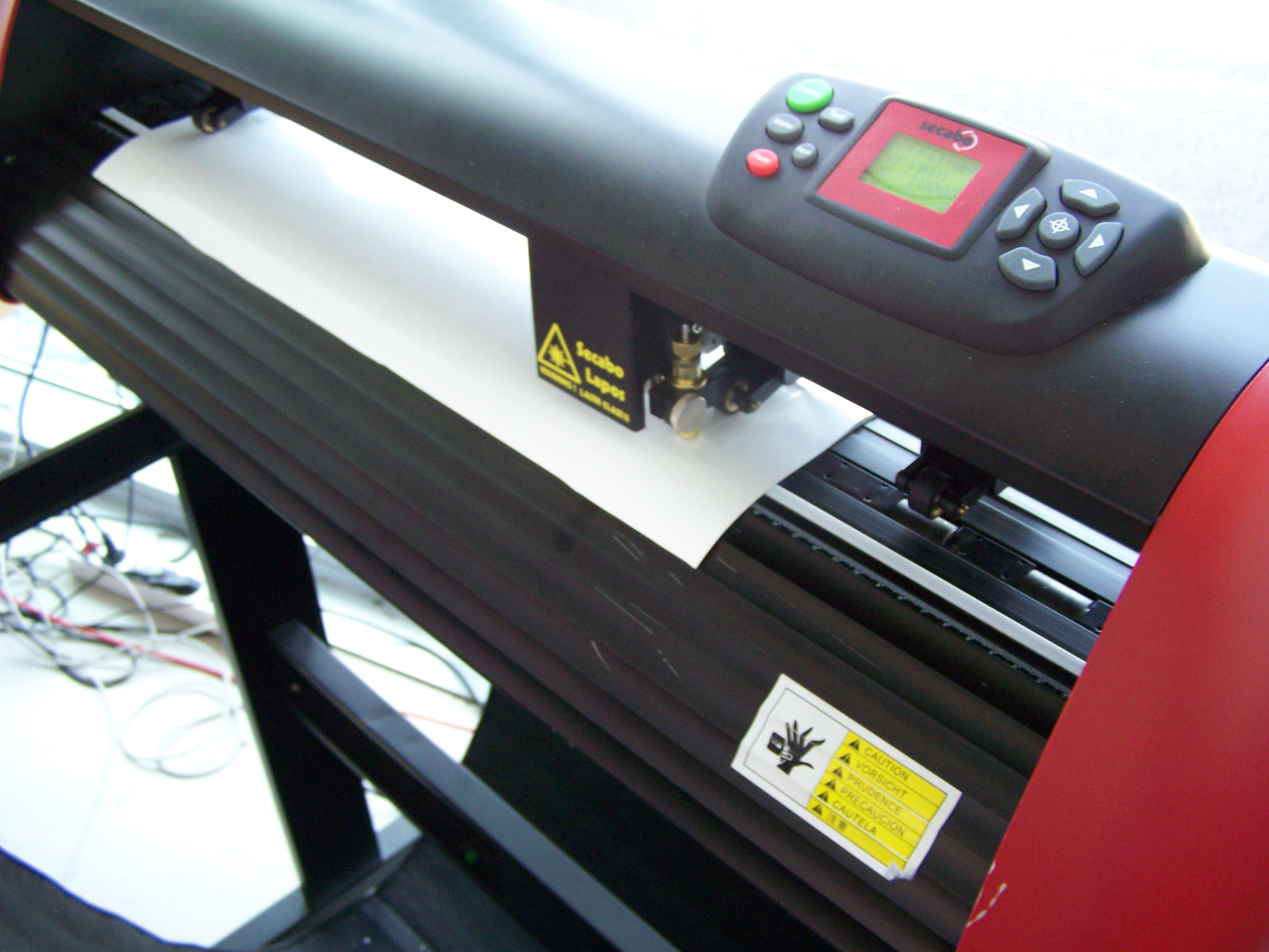 Secabo-Schneideplotter mit eingelegter weißer Folie, Schneidkopf mit Messer und Bedienfeld mit Display zum Zuschneiden von Textilfolien
