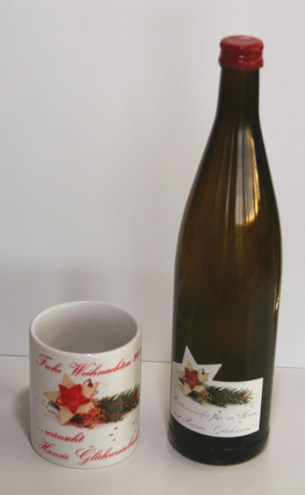Glühweinflasche mit selbst geplottetem Etikett mit Tannenzweig und Stern, daneben passende Tasse mit Weihnachtsgruß von Hansis Glühwein
