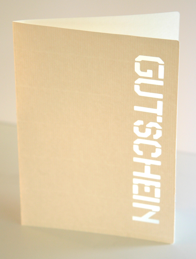 Gefaltete beige Karte mit ausgeplottetem Schriftzug GUTSCHEIN in Schablonenschrift, darunter hell schimmernder Innenkarton