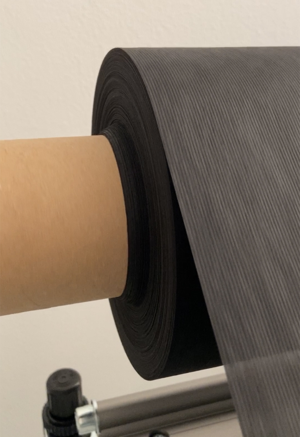 Schwarzer Vliesstoff für Gesichtsmasken auf Papphülse, die Materialbahn läuft von der Rolle an der NEPATA-Maschine