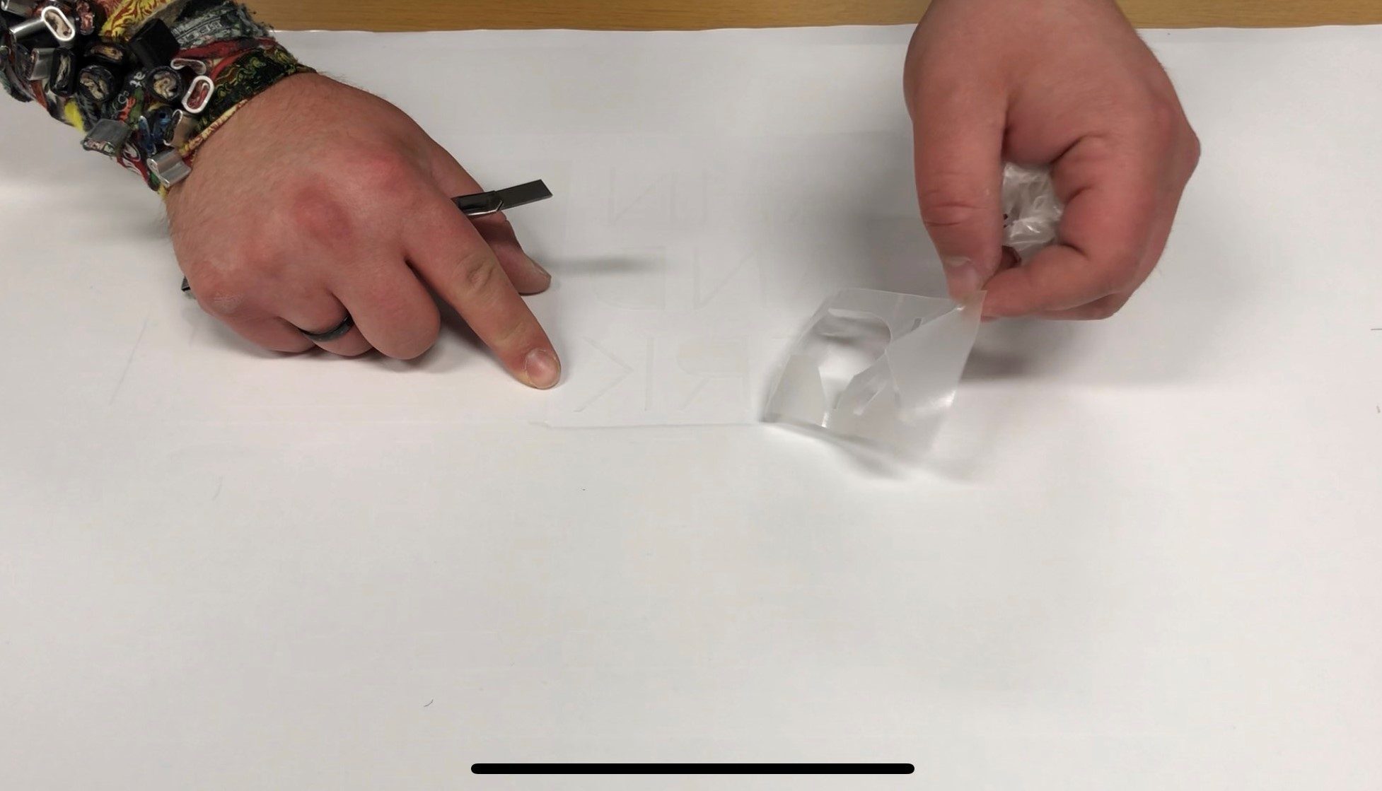 Hände entgittern geplottete Buchstaben aus Milchglasfolie, rechts wird überschüssige Folie abgezogen, links liegt eine Entgitterpinzette