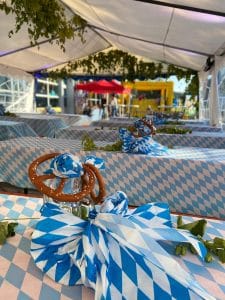Festzelt der Nepata Wiesn 2021 mit weiß-blauen Rautentischdecken, Breze und Schleifen als Tischdeko, im Hintergrund sonniger Außenbereich
