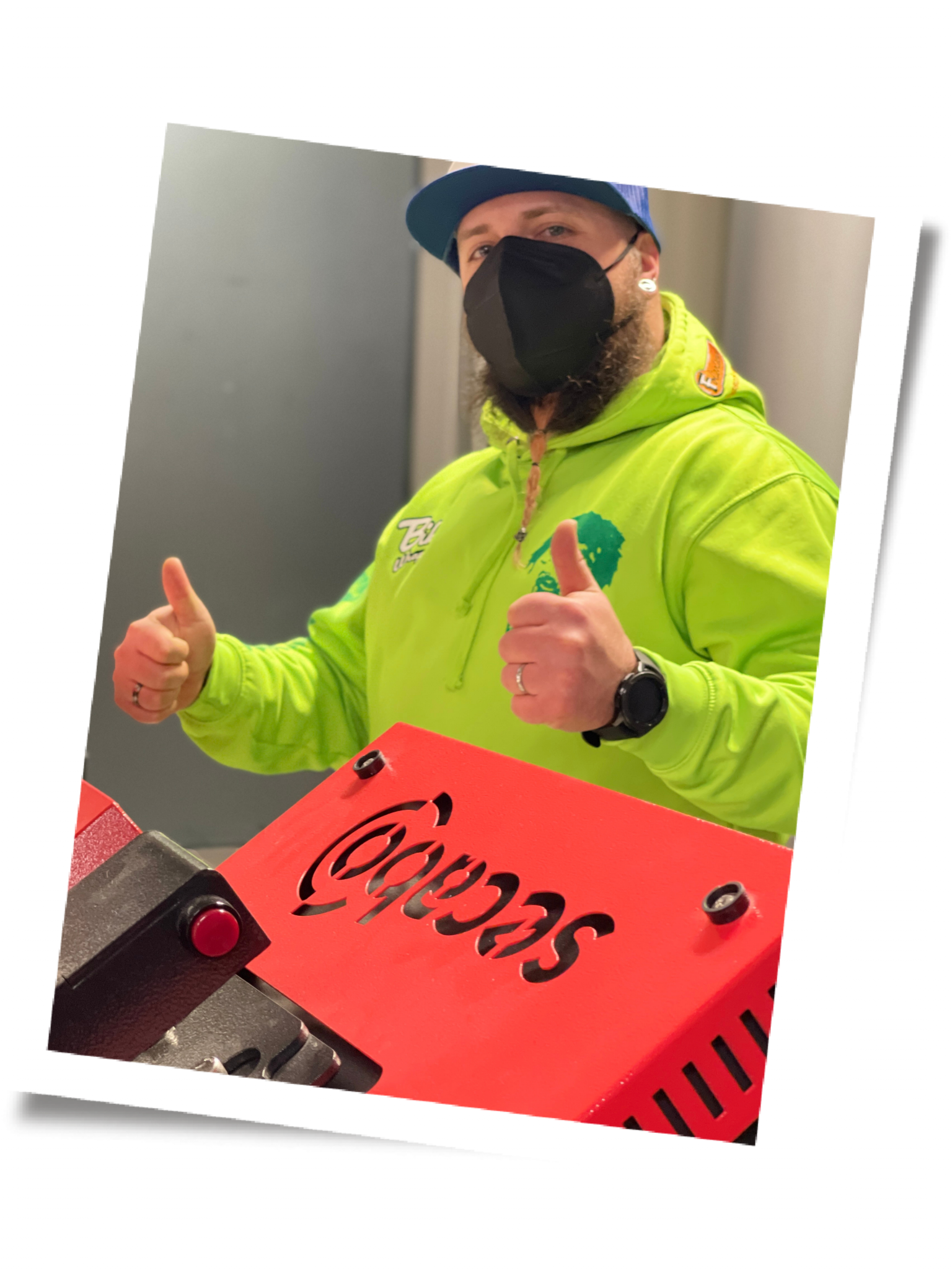 Mann mit Kappe, FFP2-Maske und neongrünem Hoodie zeigt beide Daumen hoch hinter einer roten Secabo Transferpresse