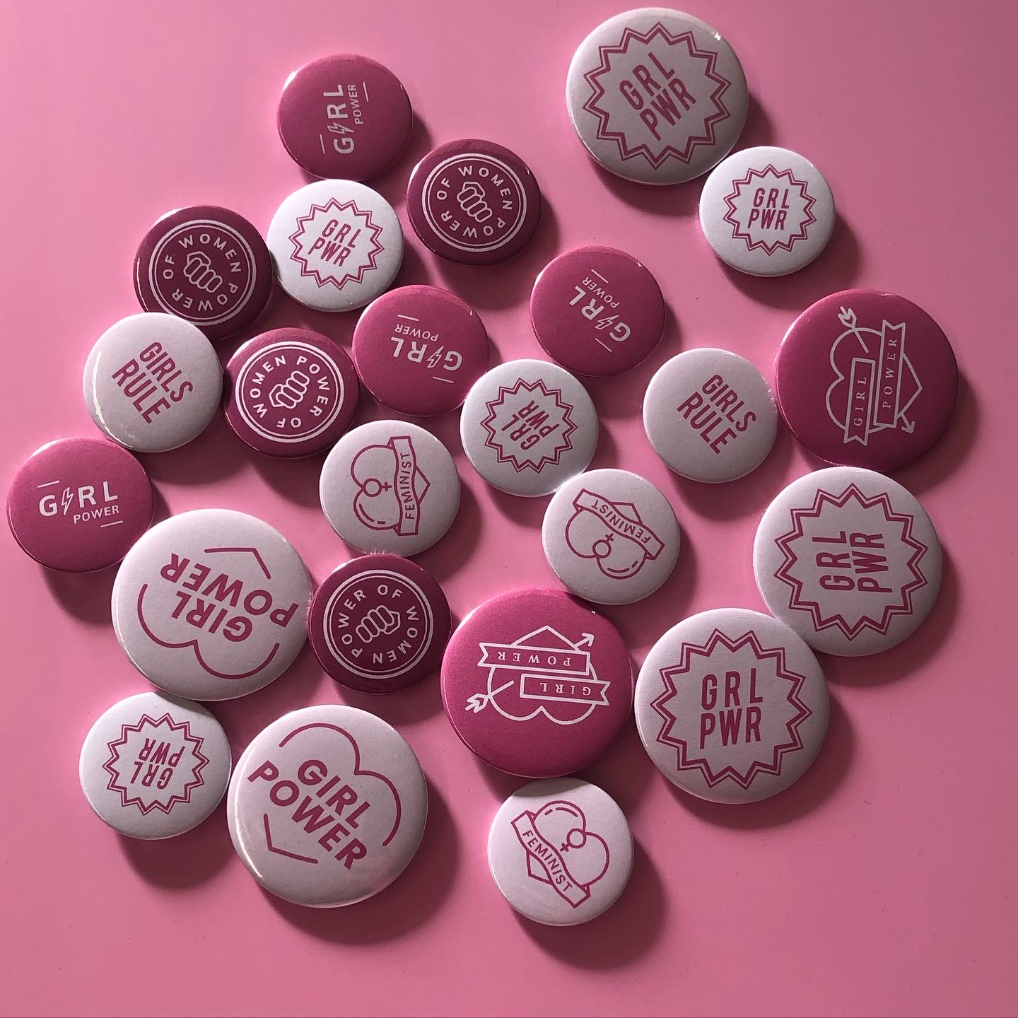 Selbst gemachte Buttons in Pink und Weiß mit Sprüchen wie Girls Rule, GRL PWR, Girl Power und Feminist auf rosa Untergrund