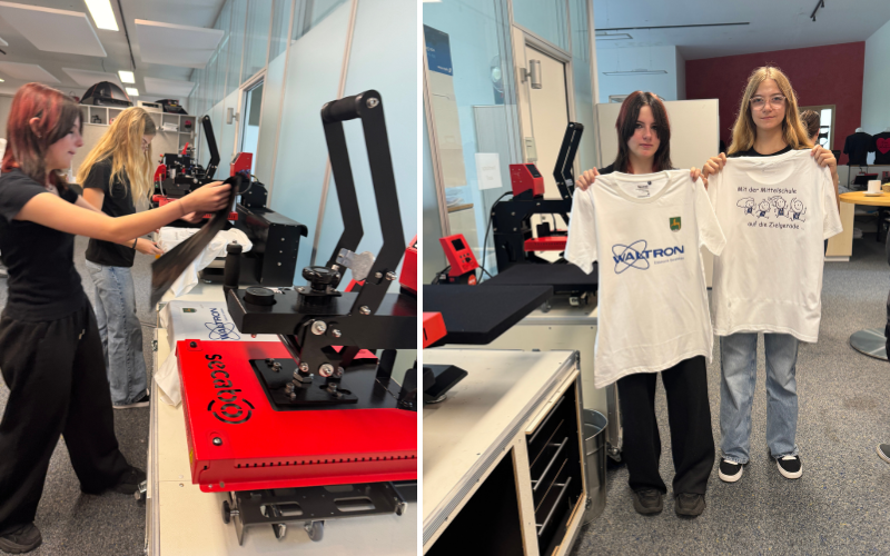 Schülerinnen bedienen die Transferpresse Secabo TD7 LITE und zeigen danach bedruckte weiße T-Shirts mit Waltron-Logo und Schulmotiv