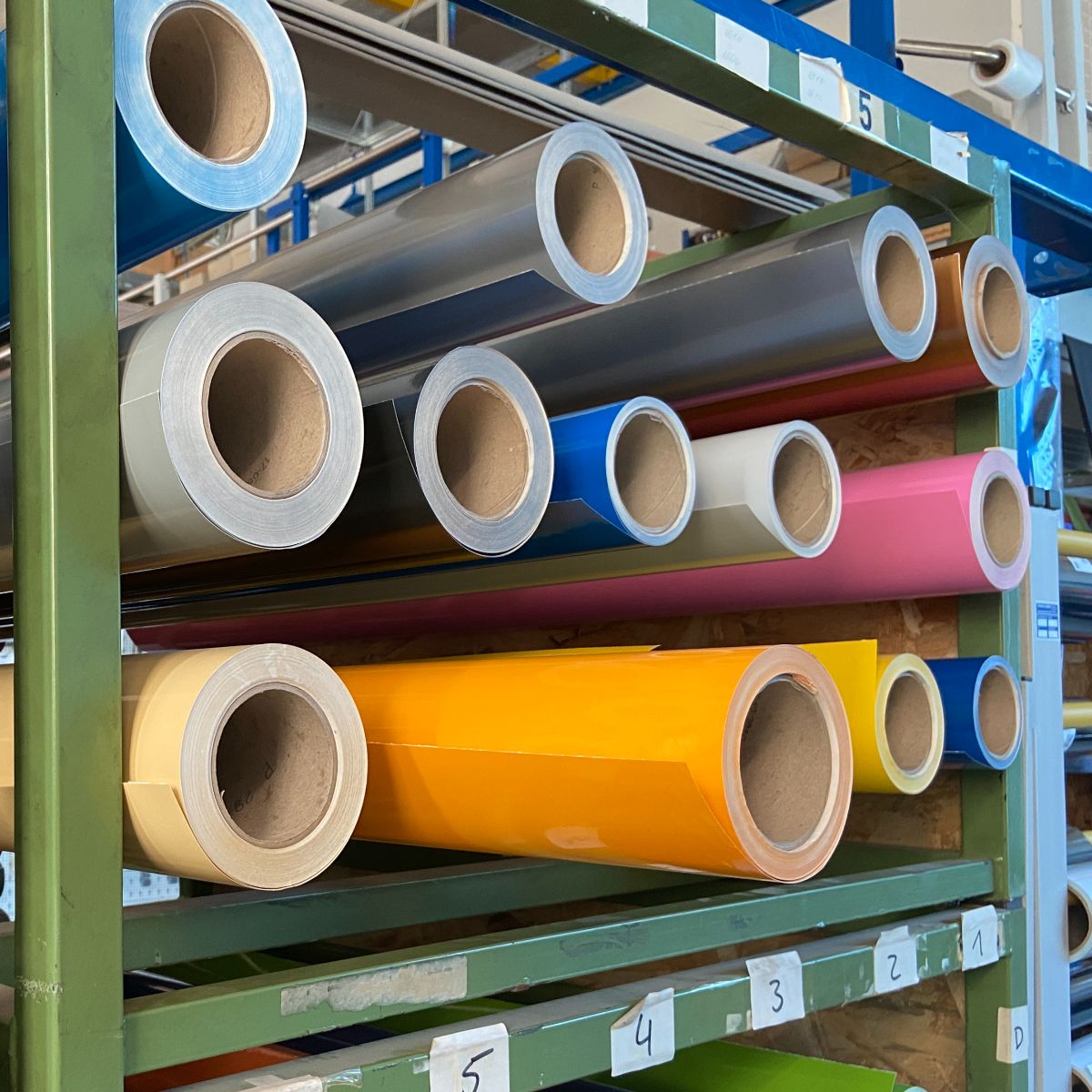 Étagère de stockage verte contenant des Rouleaux de films vinyle argentés, bleus, roses, orange et jaunes ; les compartiments sont numérotés de 1 à 5