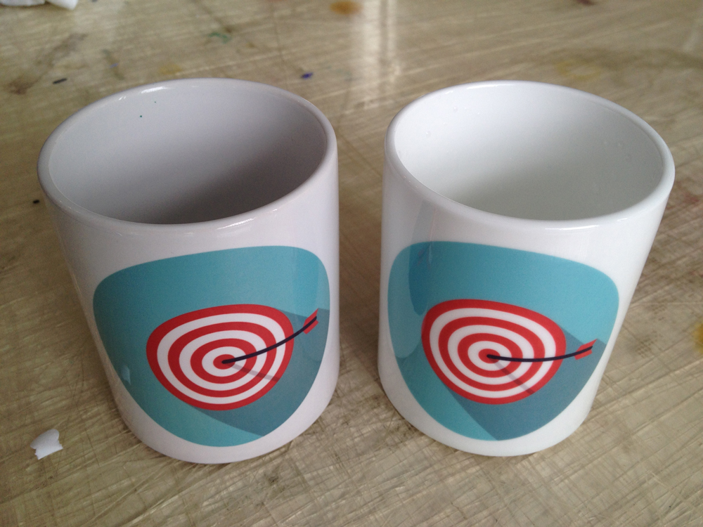 Zwei sublimierte Tassen mit Zielscheiben-Motiv: links Standard-A-Tasse mit gräulicher Innenseite, rechts reinweiße AAA ORCA Tasse