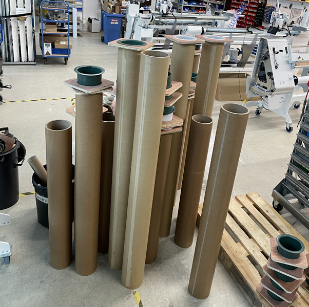 Des tubes en carton de 6 pouces posés debout, dont certains sont munis de capuchons en plastique verts, dans l'atelier ; à l'arrière-plan, des dérouleuses NEPATA