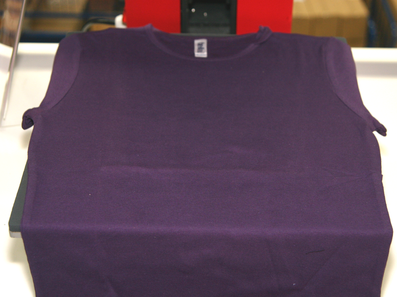 Lila T-Shirt glatt auf der Unterplatte einer roten Transferpresse eingelegt, bereit zum Aufpressen des Strass-Motivs