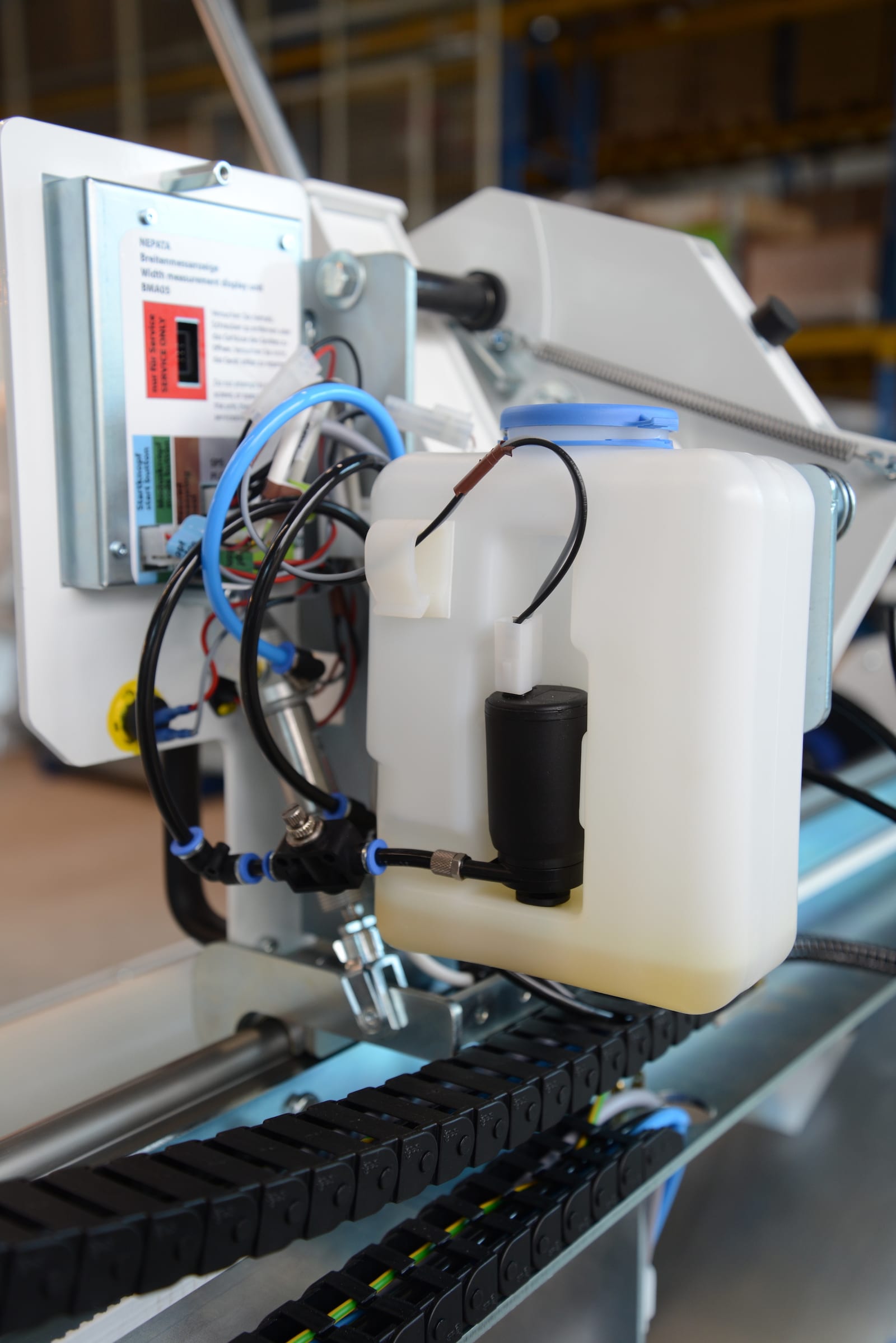 Tank des automatischen NEPATA-Backenschmiersystems mit Pumpe und Schläuchen, montiert an einer Abstechmaschine, teils mit Schmiermittel gefüllt