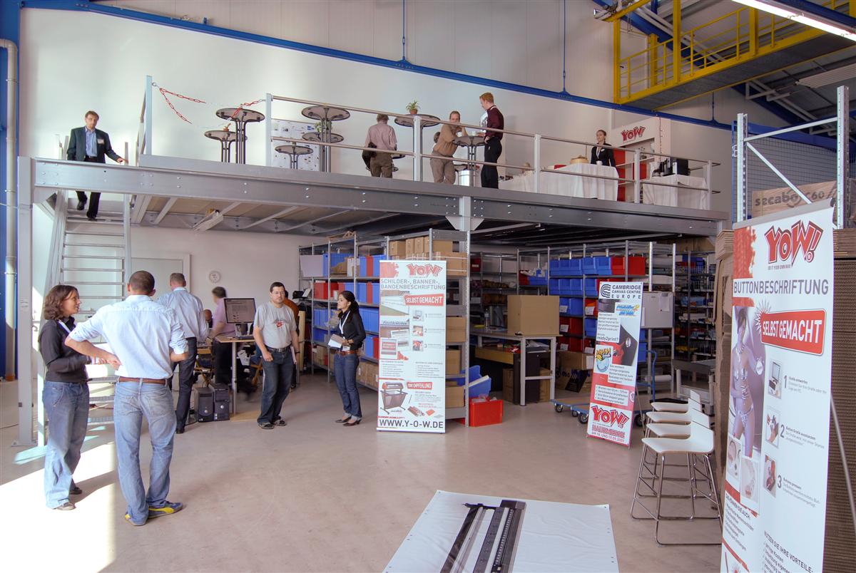Hausmesse bei YOW! in Wolnzach: Besucher in der Lagerhalle zwischen Roll-ups, Regalen und Stehtischen auf der Empore, Mitarbeiter beraten