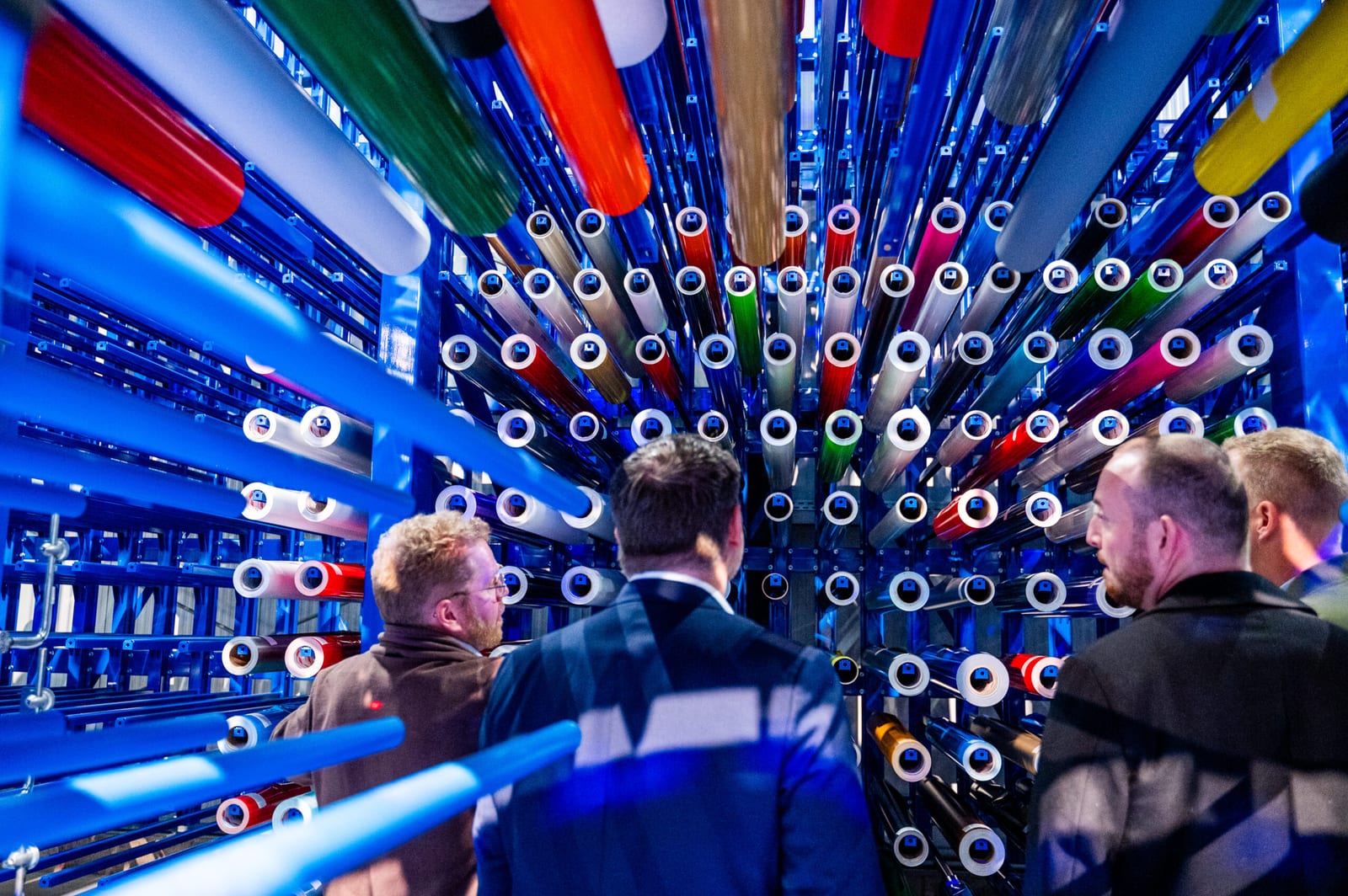 Les invités de la soirée d'inauguration admirent, dans le système de rayonnages bleus Nepata ARSS installé chez 4 GM à Trèves, les nombreux Rouleaux de films vinyle stockés dans une grande variété de couleurs.