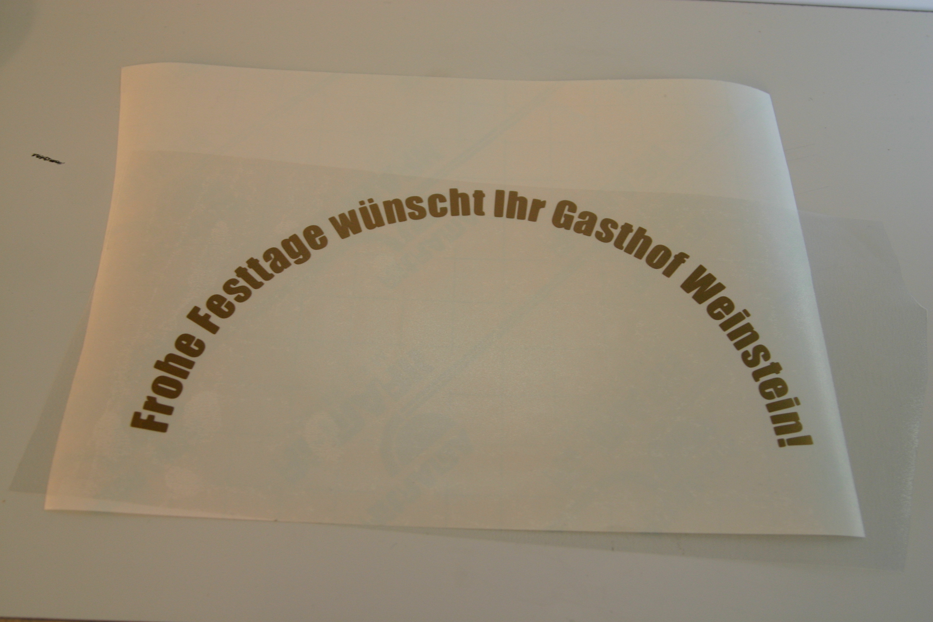 Goldener Folienschriftzug im Bogen „Frohe Festtage wünscht Ihr Gasthof Weinstein!“, geplottet und entgittert, mit Übertragungsfolie auf Trägerpapier