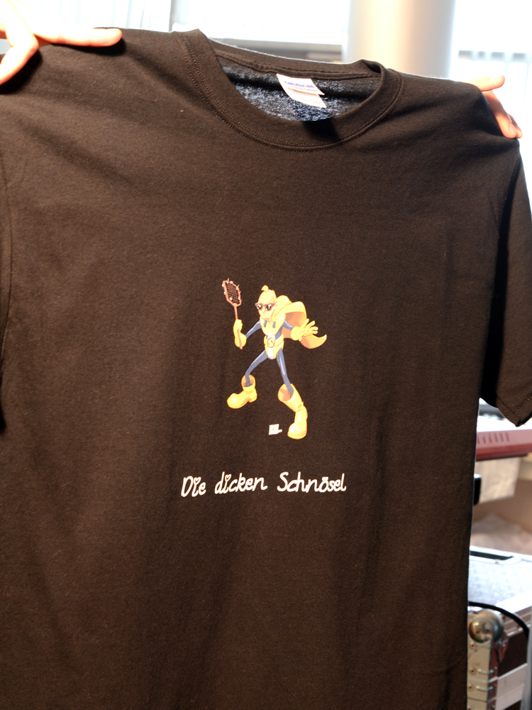 Fertiges schwarzes Band-Shirt mit vollfarbiger Comicfigur mit Fliegenklatsche und weißem Schriftzug Die dicken Schnösel per READY Transfer