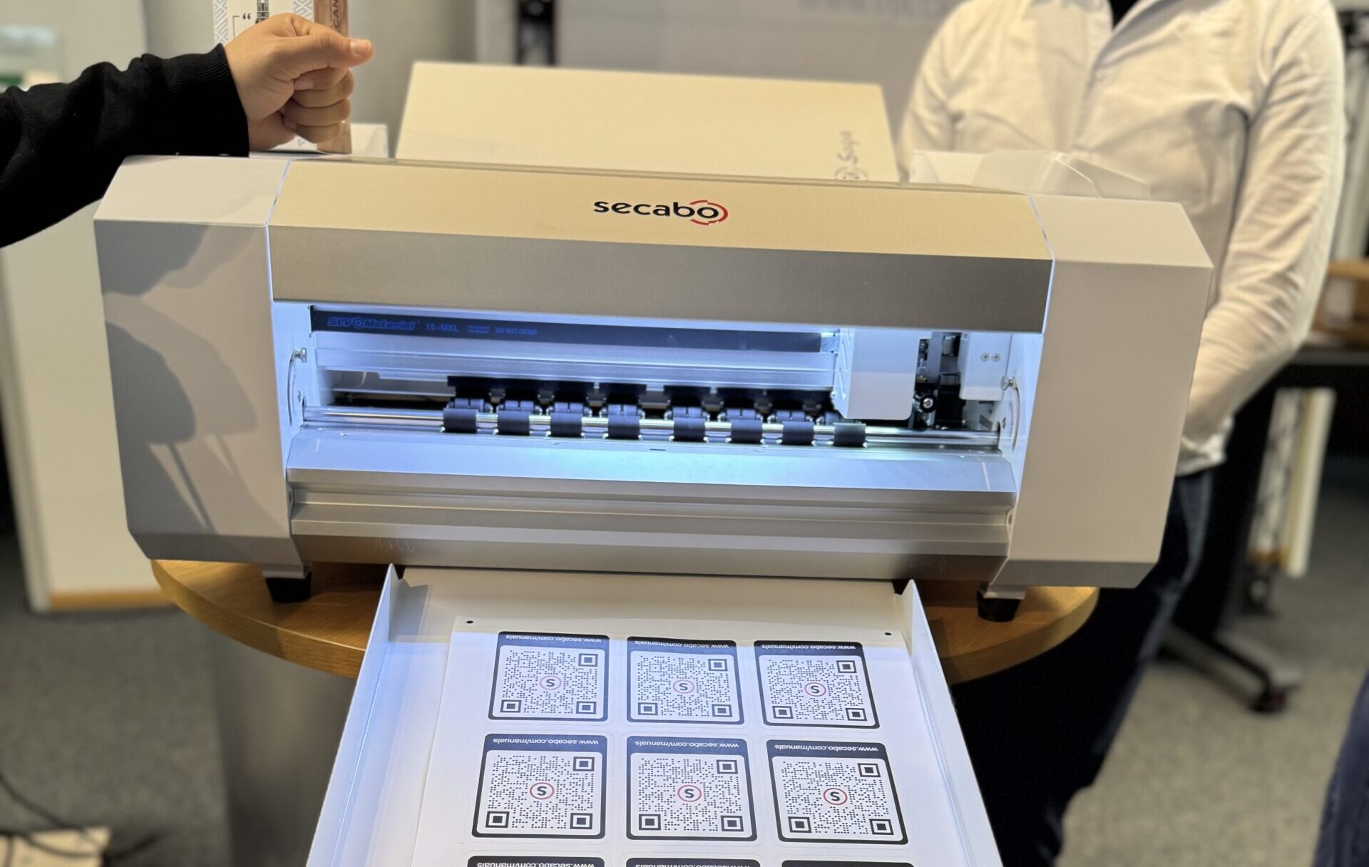 Secabo SC30 II Bogenschneideplotter, im Ausgabefach ein Bogen mit konturgeschnittenen QR-Code-Stickern
