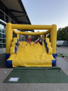 Kinder rutschen auf einer gelben Hüpfburg vor dem gläsernen Firmengebäude, Kinderprogramm bei der Nepata Wiesn 2021