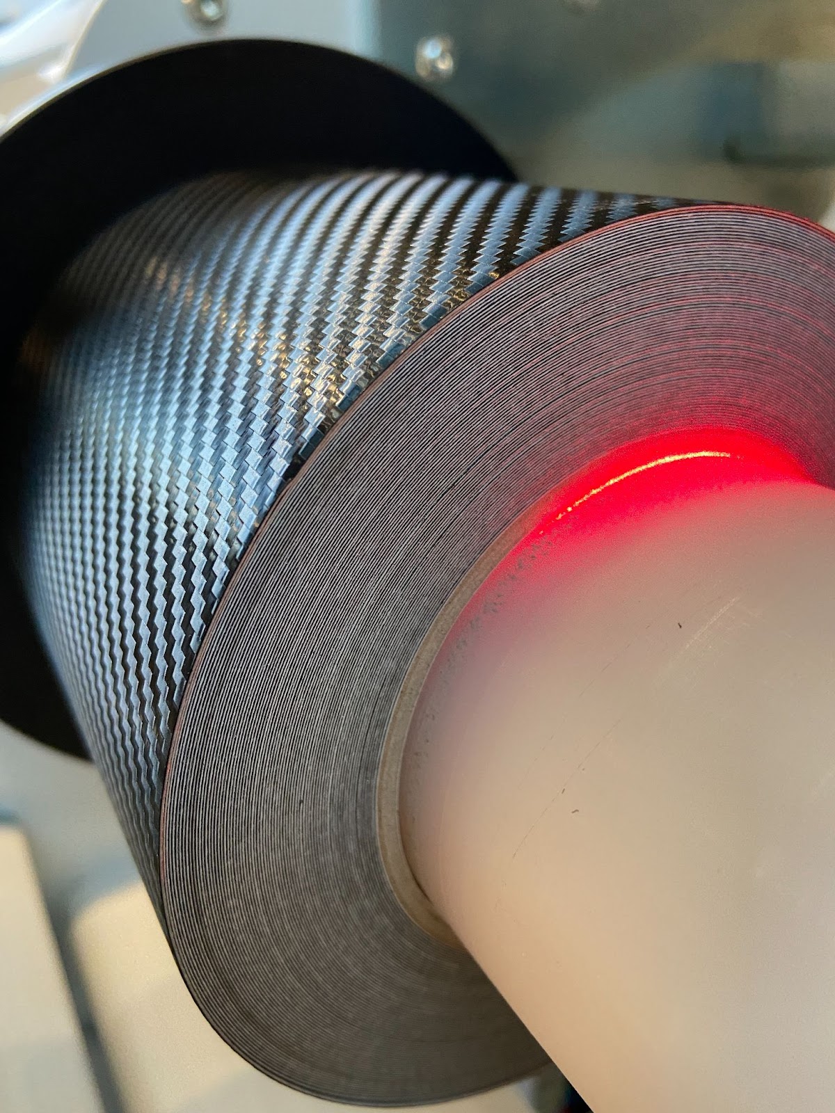 Rolle gegossener Carbonfolie in der Abstechmaschine, Schnittkante mit sauber gewickelten Lagen, roter Laser markiert die Schnittposition