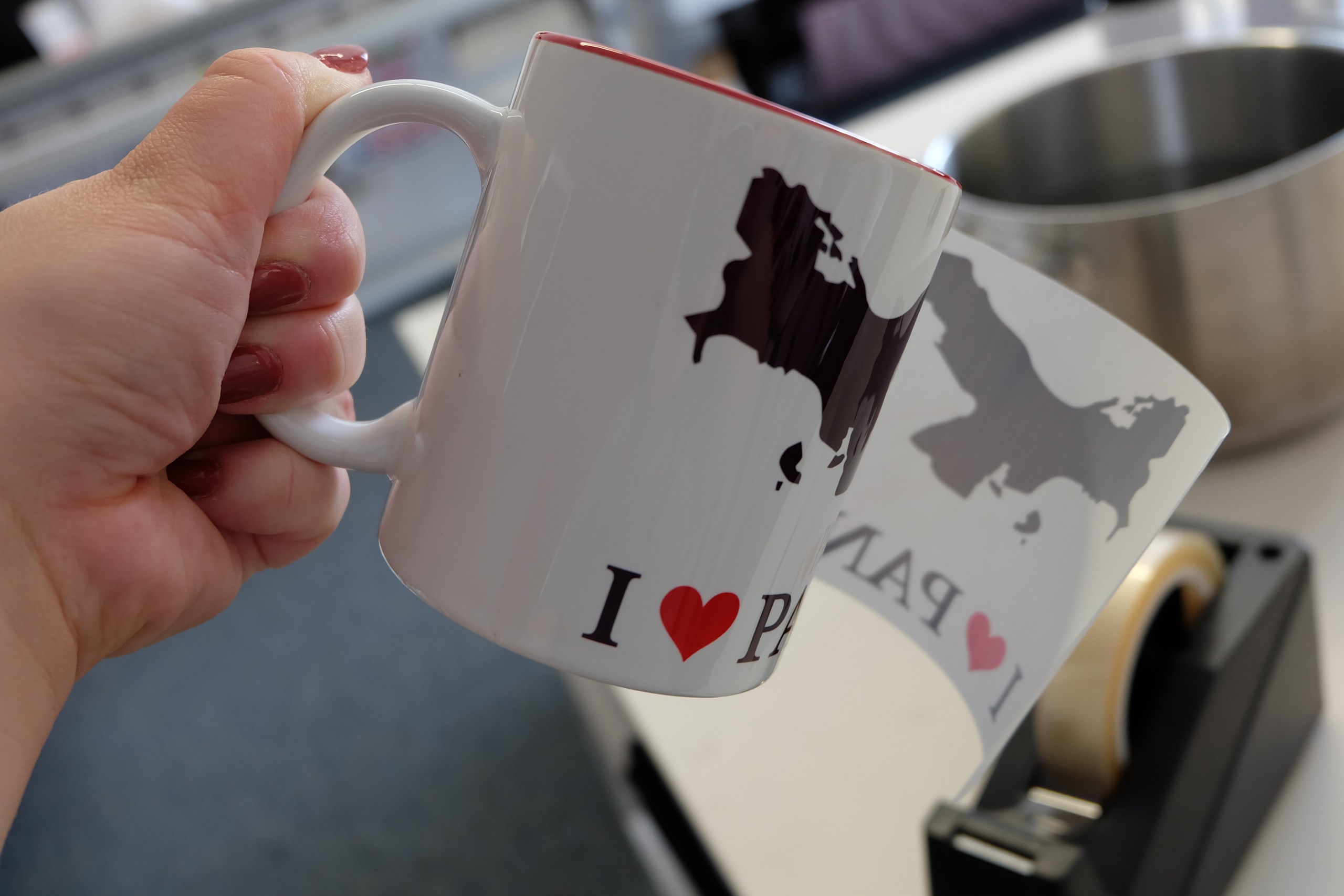 Transferpapier wird von frisch gepresster Tasse mit Karte und I ♥ Panama abgezogen, dahinter Wassertopf zum Abschrecken