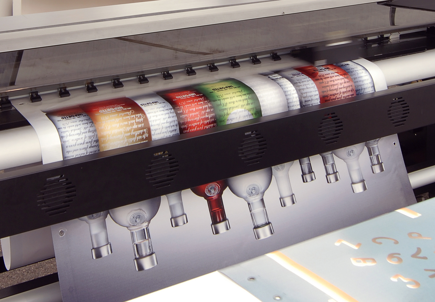 Großformatdrucker bedruckt weißes Bannermaterial mit Motiv aus Flaschen und farbigen Etiketten, Beispiel für digitalen Bannerdruck