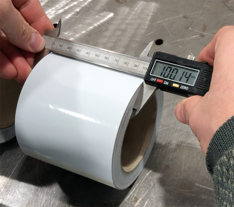 Digitaler Messschieber zeigt 100,14 mm an abgestochener weißer Rolle Ritrama Klebefolie, Abweichung vom Sollmaß unter 0,2 mm