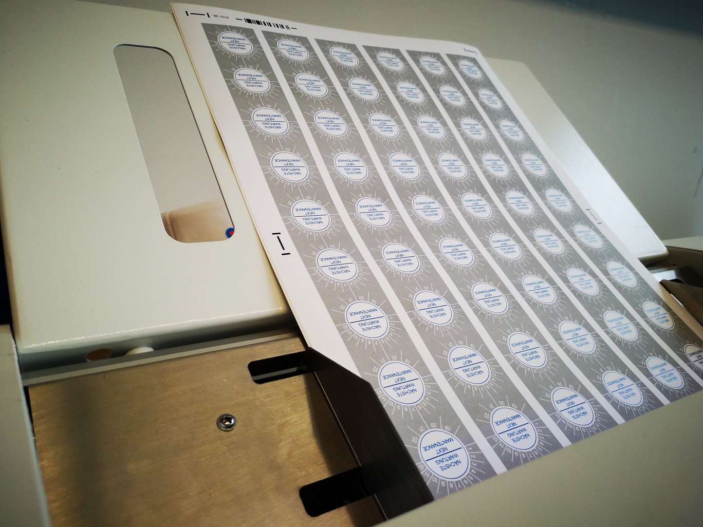 Bedruckter Klebefolienbogen mit Wartungsplaketten Nächste Wartung und Positionsmarken in der Papierzufuhr des Schneideplotters SC30