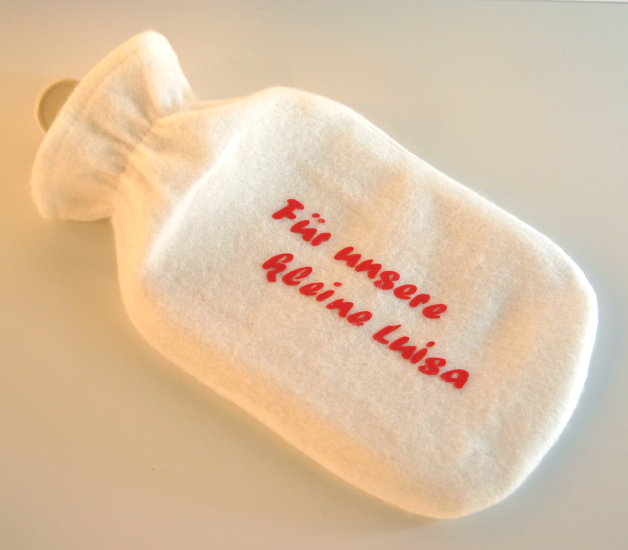 Wärmflasche mit weißem Fleecebezug, beklebt mit rotem Flockfolien-Schriftzug Für unsere kleine Luisa – das fertige DIY-Ergebnis