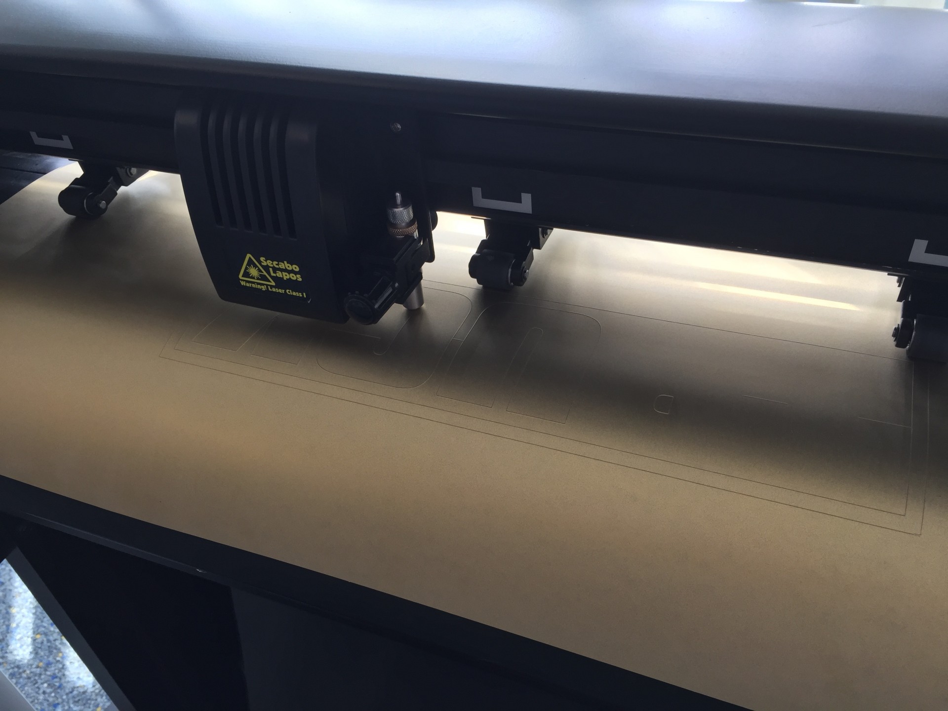 Schneidkopf des Secabo T60 schneidet einen Schriftzug mit umlaufendem Entgitterrahmen in goldene Flexfolie von Selectsign