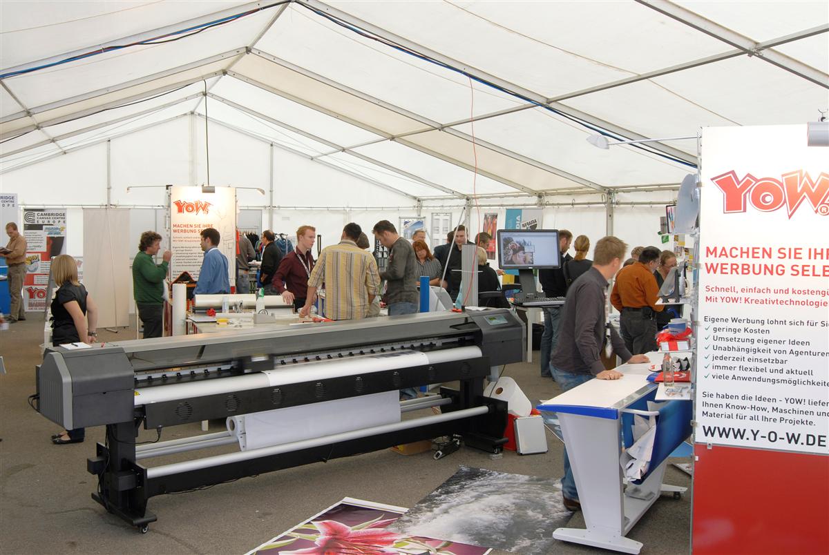 Besucher der YOW!-Hausmesse 2009 in Wolnzach im Messezelt, vorne ein Großformatdrucker, rechts Banner Machen Sie Ihre Werbung selbst