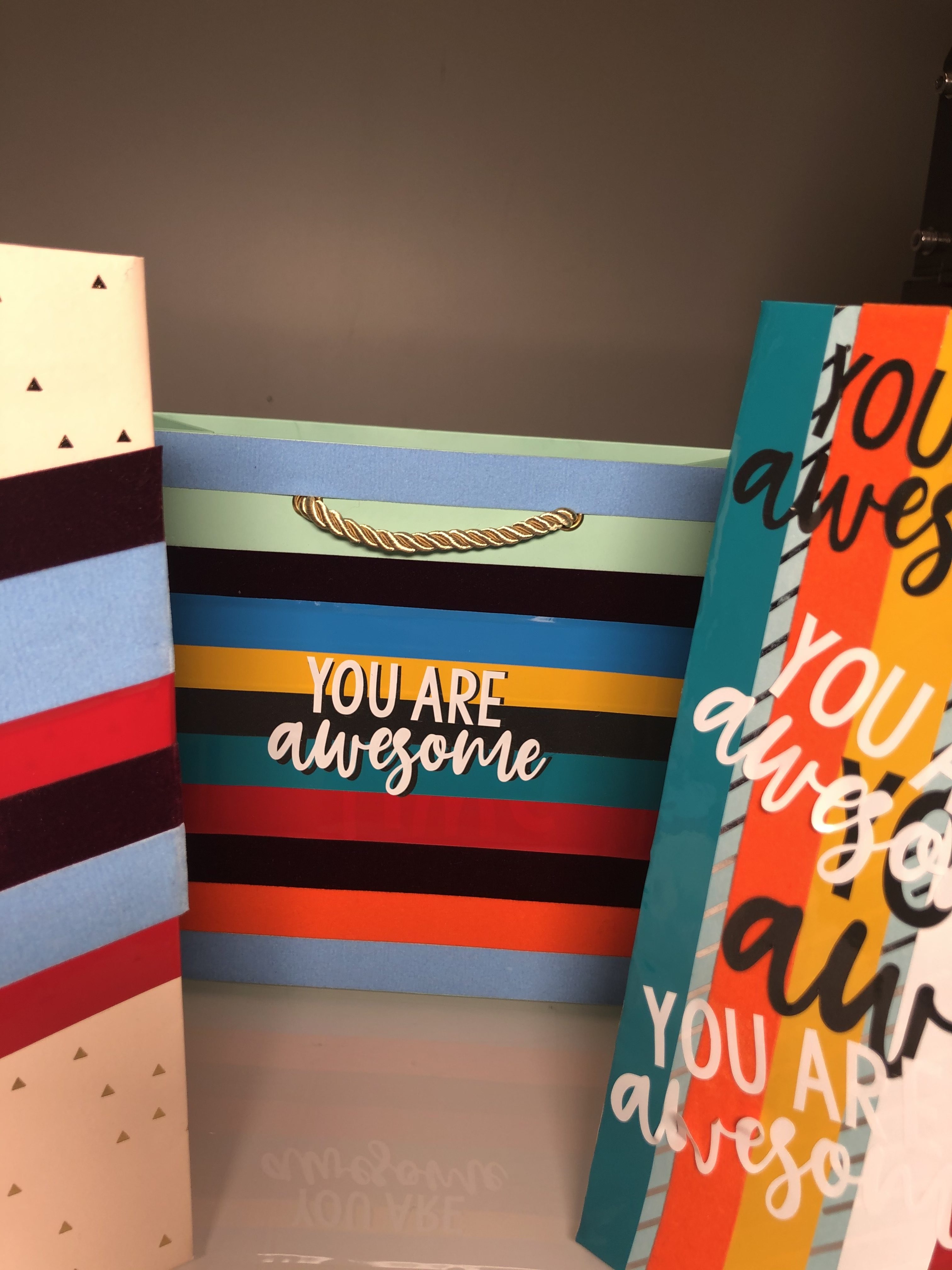 Geschenktüte mit bunten Streifen aus Flock- und Glanzfolie und weißem Schriftzug YOU ARE awesome, daneben weitere so beklebte Tüten