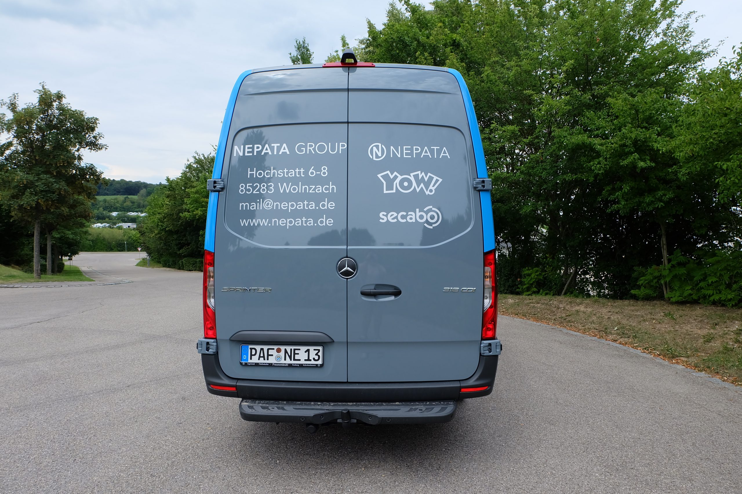 Heck eines grauen Mercedes Sprinter mit weißer Beklebung auf den Hecktürscheiben: Nepata-Group-Adresse und Logos von Nepata, YOW! und secabo