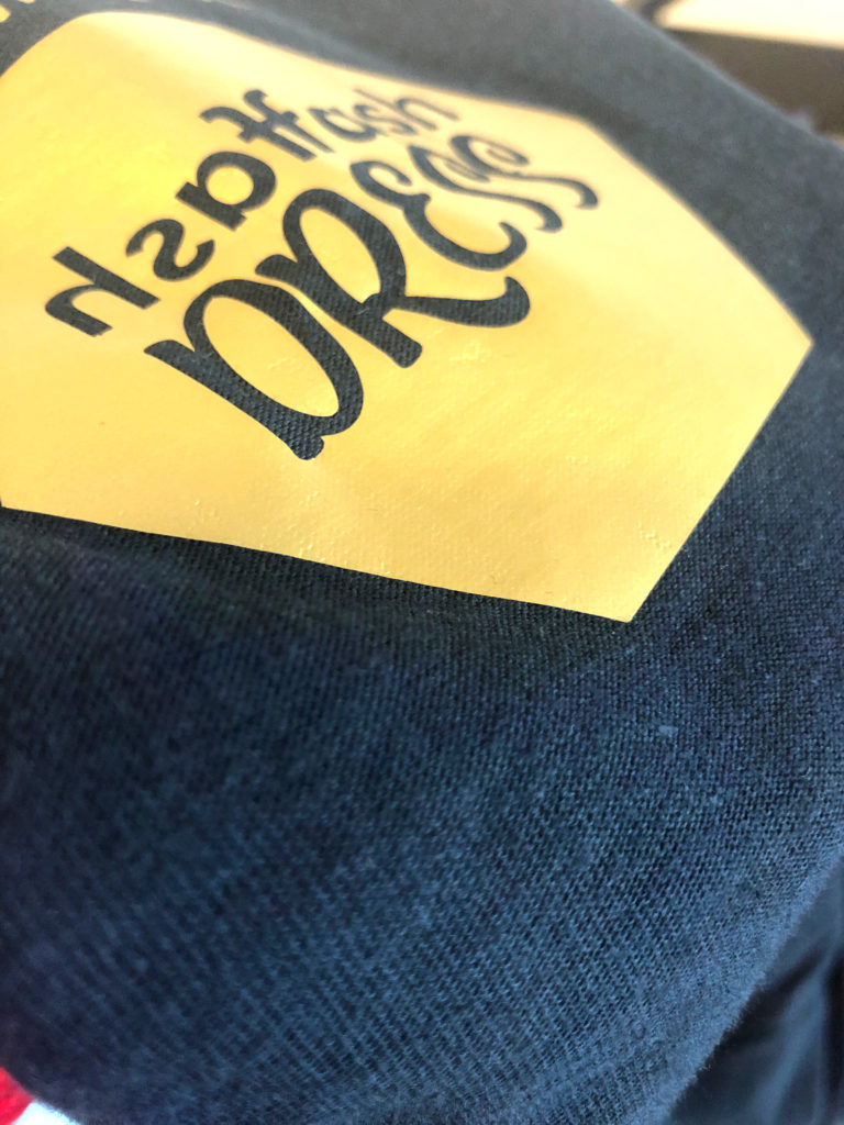 Nahaufnahme eines dunkelblauen Shirts mit gelbem Transfermotiv mit schwarzer Schrift, aufgebracht mit der Secabo TC1 ohne Sublimation