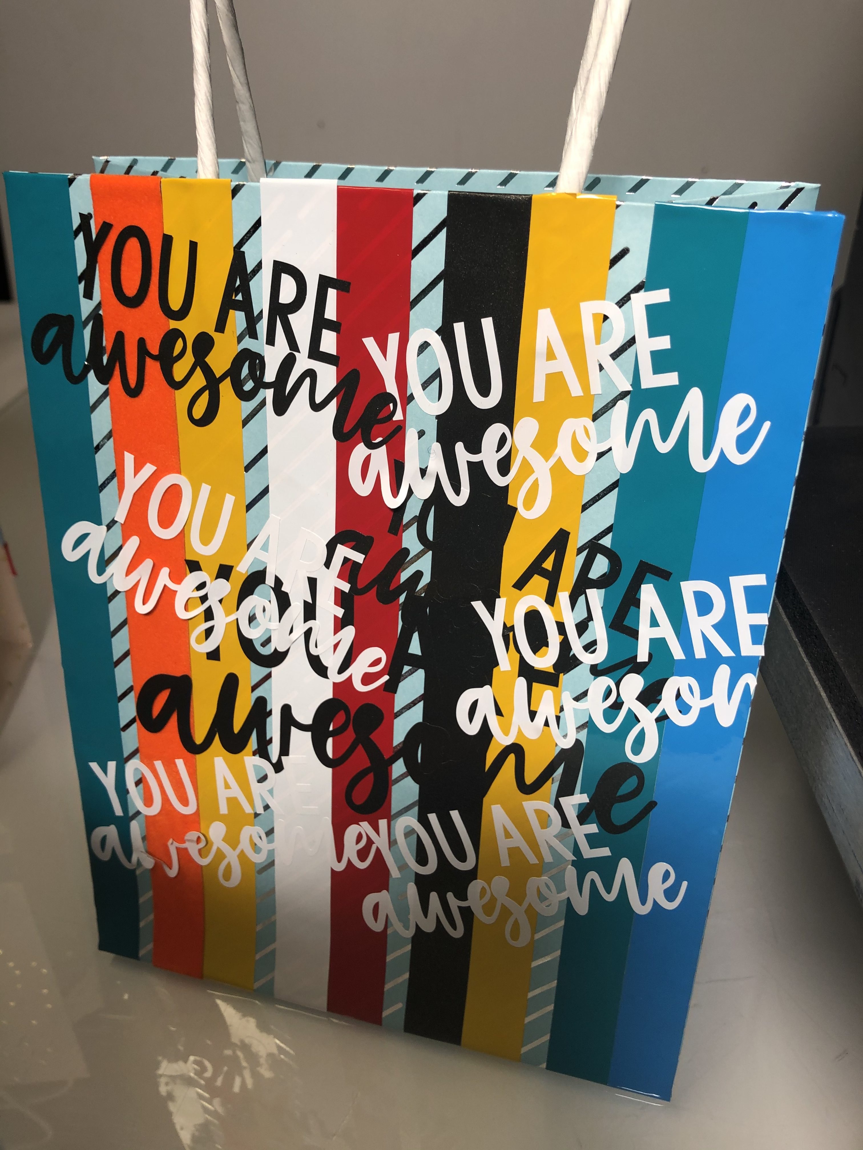 Hellblaue Geschenktüte, beklebt mit bunten Folienstreifen und Schriftzügen You are awesome aus weißer und schwarzer Selbstklebefolie