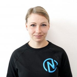 Porträt von Stefanie Hartleitner, neue Mitarbeiterin in der Bauteilmontage, mit zurückgebundenem blondem Haar in schwarzem Pullover mit blauem Firmenlogo