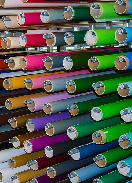 De nombreux rouleaux de films vinyle de toutes les couleurs sont rangés les uns à côté des autres sur une étagère – symbole de la grande diversité de produits proposés dans le commerce des films vinyle