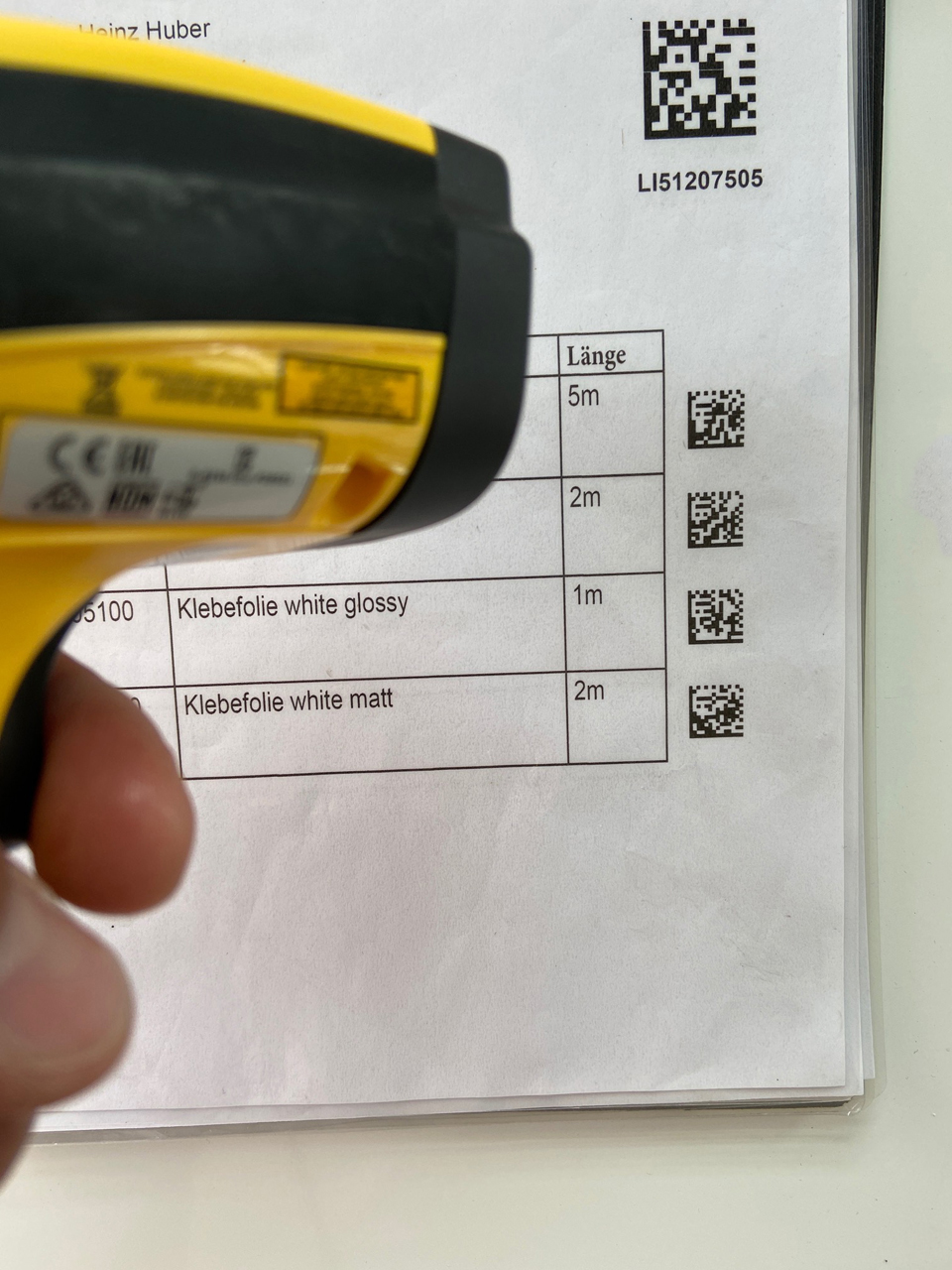 Gelber Handscanner vor Lieferschein mit 2D-Codes neben Folienpositionen und Längen zum Einlesen des Auftrags in ConvertPlus2