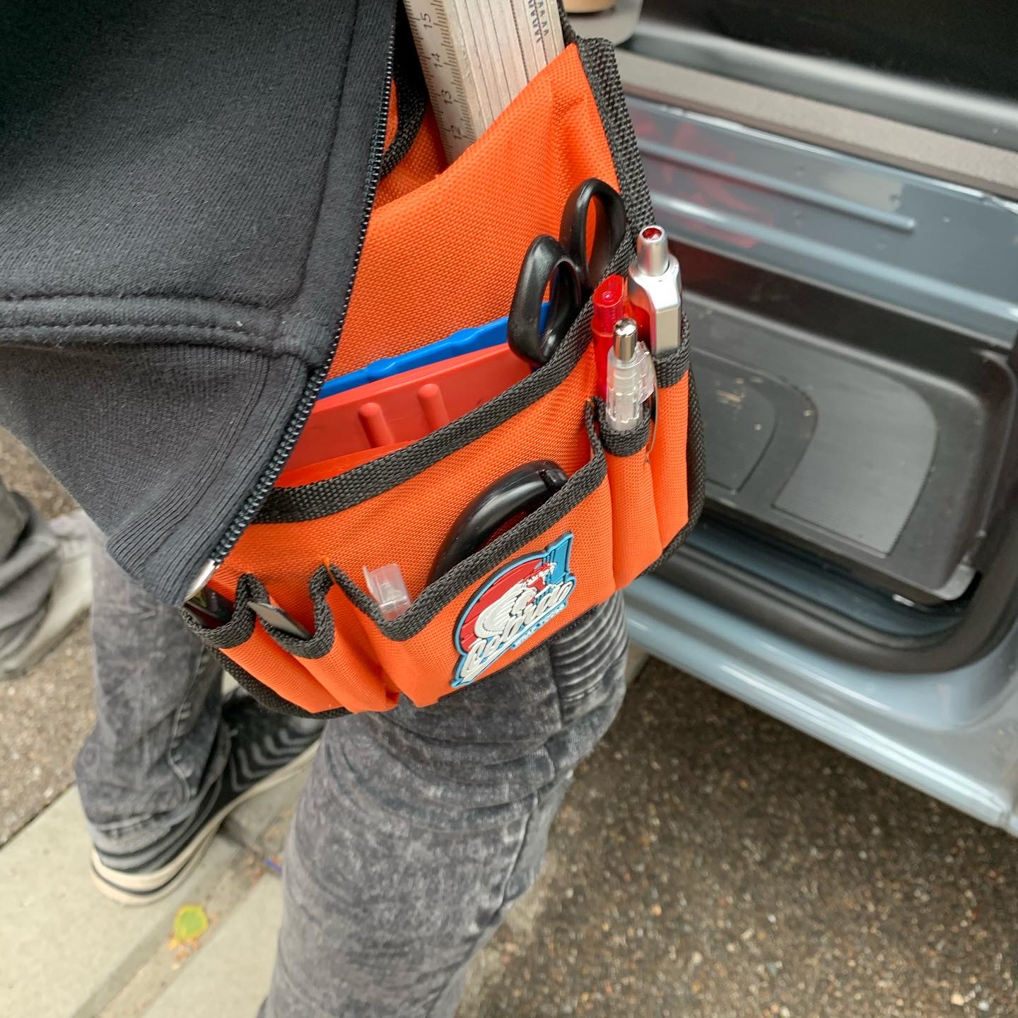 Orange Werkzeugtasche am Gürtel mit Rakel, Schere, Cuttermesser, Zollstock und Stiften, Werkzeug zum Verkleben von Selbstklebefolie