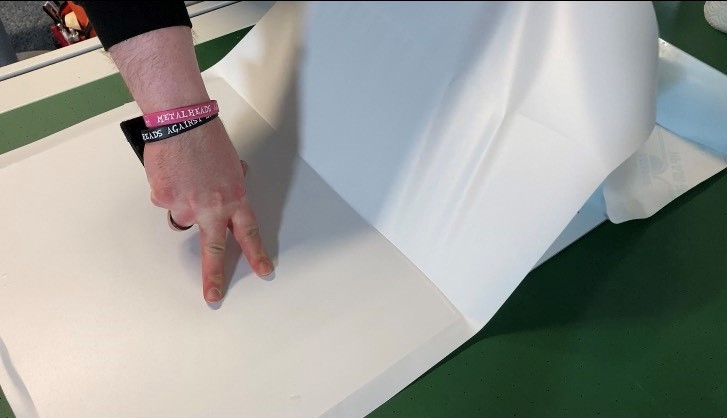 Hand streicht weiße Selbstklebefolie auf ein Schild, um es vollflächig zu kaschieren, der Rest der Folie ist noch angehoben