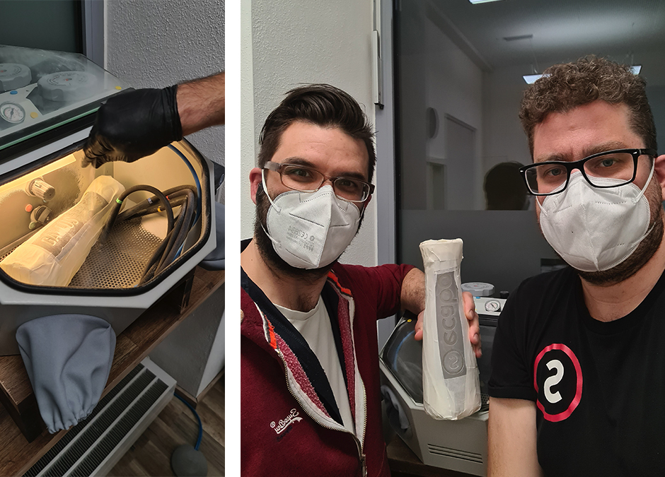 Links foliierte Karaffe in der Sandstrahlkabine, rechts zwei Männer mit FFP2-Masken halten die mit Klebefolie maskierte Karaffe
