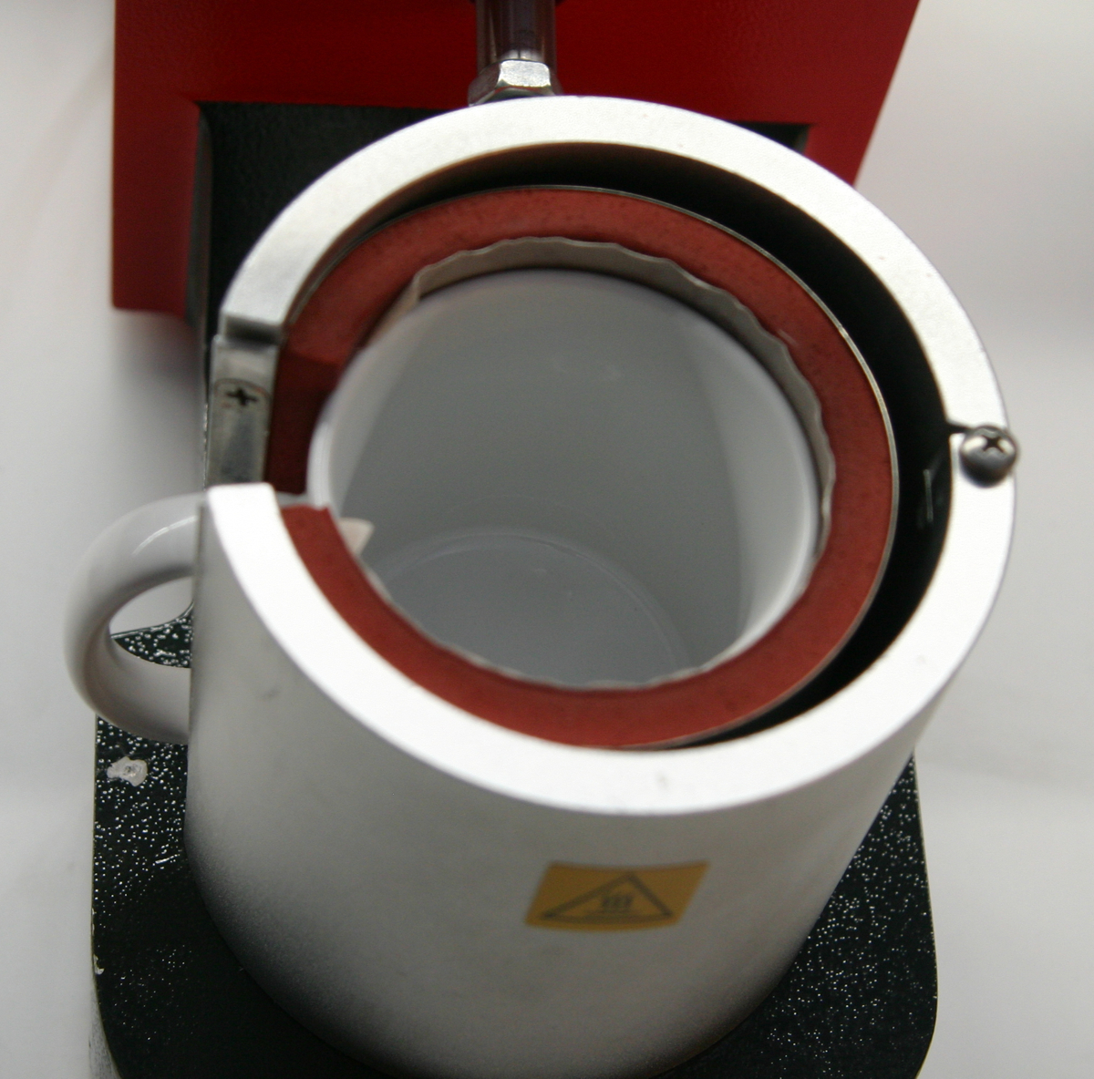 Weiße Tasse eingespannt in der silbernen Heizmanschette einer Transferpresse, Blick von oben beim Sublimieren des aufgeklebten Motivs