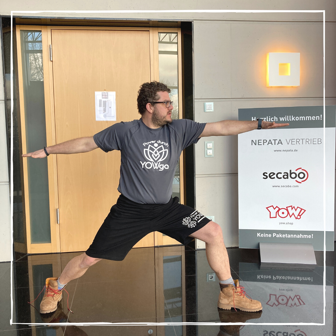Geschäftsführer Bernhard in Yoga-Kriegerpose, T-Shirt und Shorts mit geplottetem Motiv Power durch YOWga, vor dem Firmeneingang