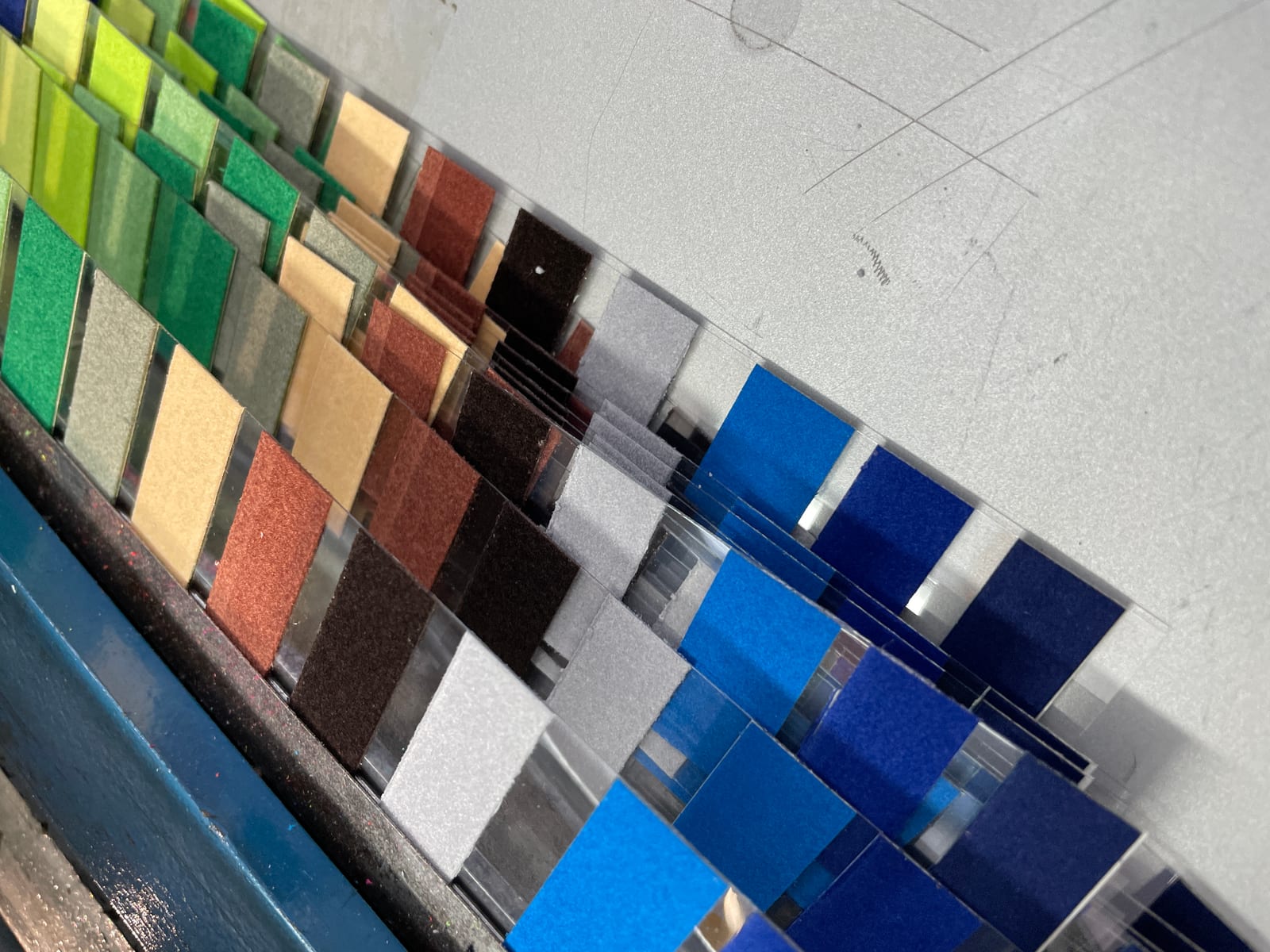 Zugeschnittene Flockfolien-Muster in Grün, Beige, Rot, Braun, Grau und Blau, reihenweise auf transparenten Trägerstreifen in der Produktion
