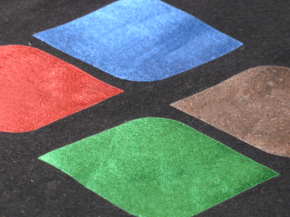 Chrom-Flexfolien in Rot, Blau, Grün und Champagner als Blattformen auf schwarzem Shirt verpresst, Stoffstruktur schimmert durch
