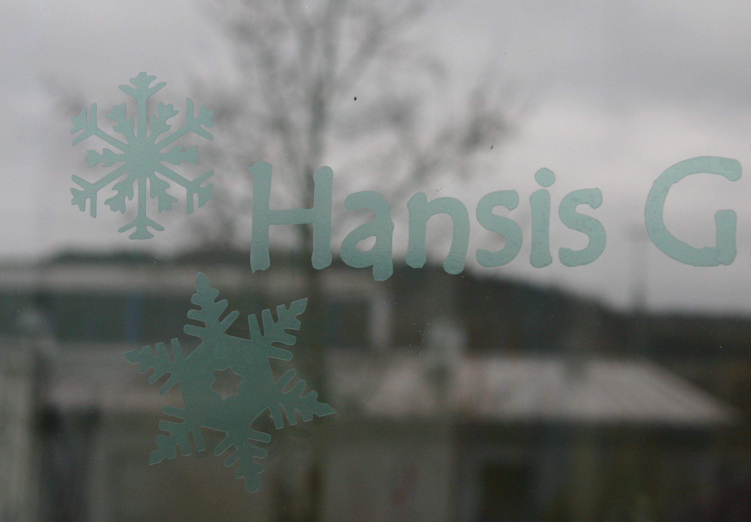 Mintgrüne Maskierfolie mit zwei geplotteten Schneeflocken und dem angeschnittenen Schriftzug Hansis G, auf eine Fensterscheibe geklebt