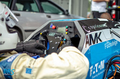 Cockpit des BRS-Motorsport-Rennwagens mit Lenkrad-Display, Fahrerhand im Handschuh und Sponsorenaufklebern wie AMK und Eaton aus Plotterfolie