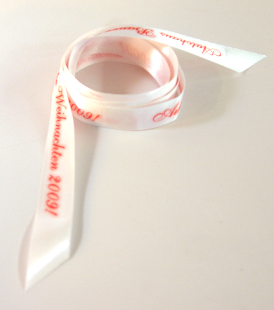 Fertig sublimiertes weißes Satin-Geschenkband, locker aufgerollt, mit rotem Schriftzug Weihnachten 2009! und dem Namen eines Autohauses