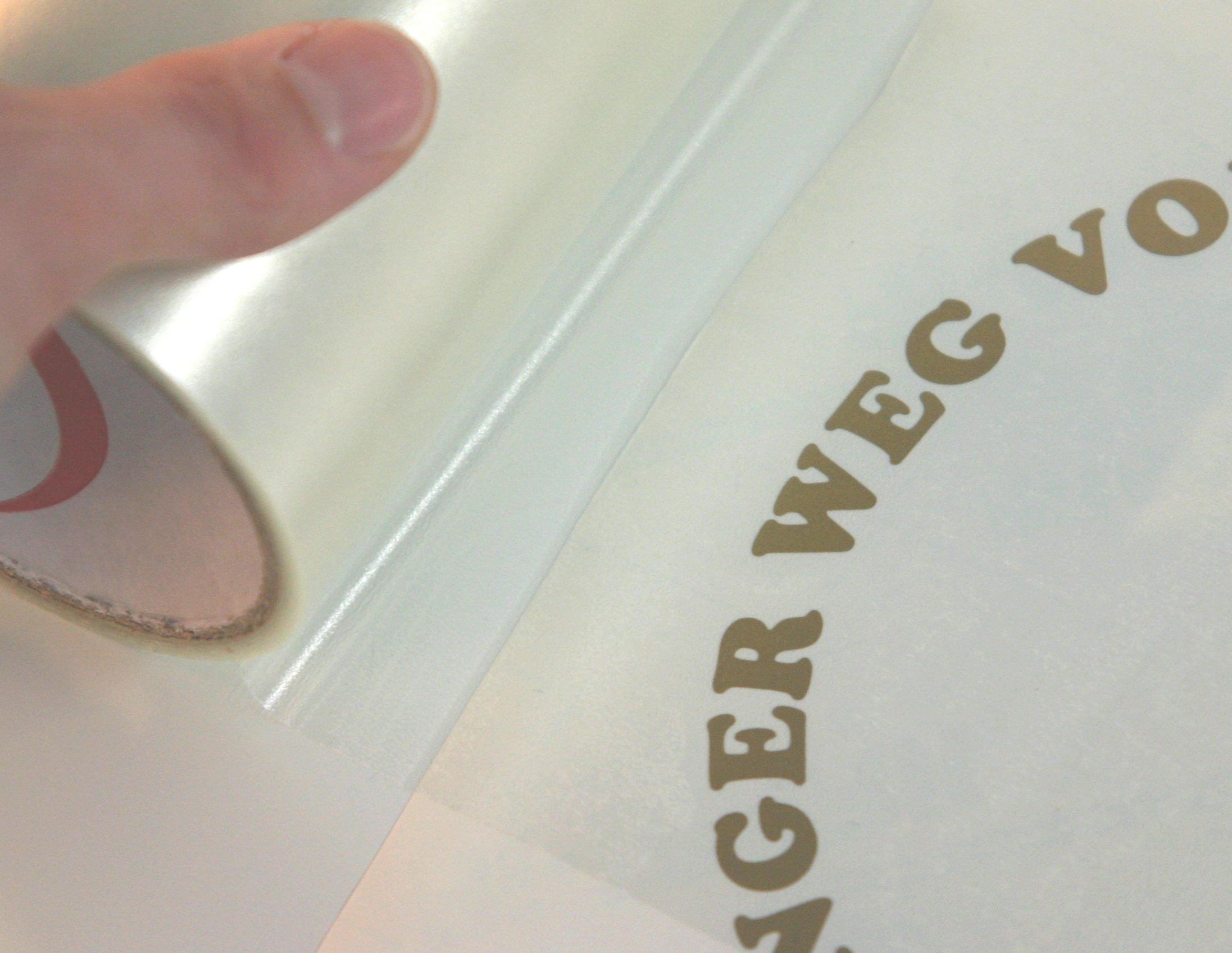 Hand rollt transparentes Applikationspapier über den geplotteten goldfarbenen Folienschriftzug …GER WEG VO… für die Plätzchendose