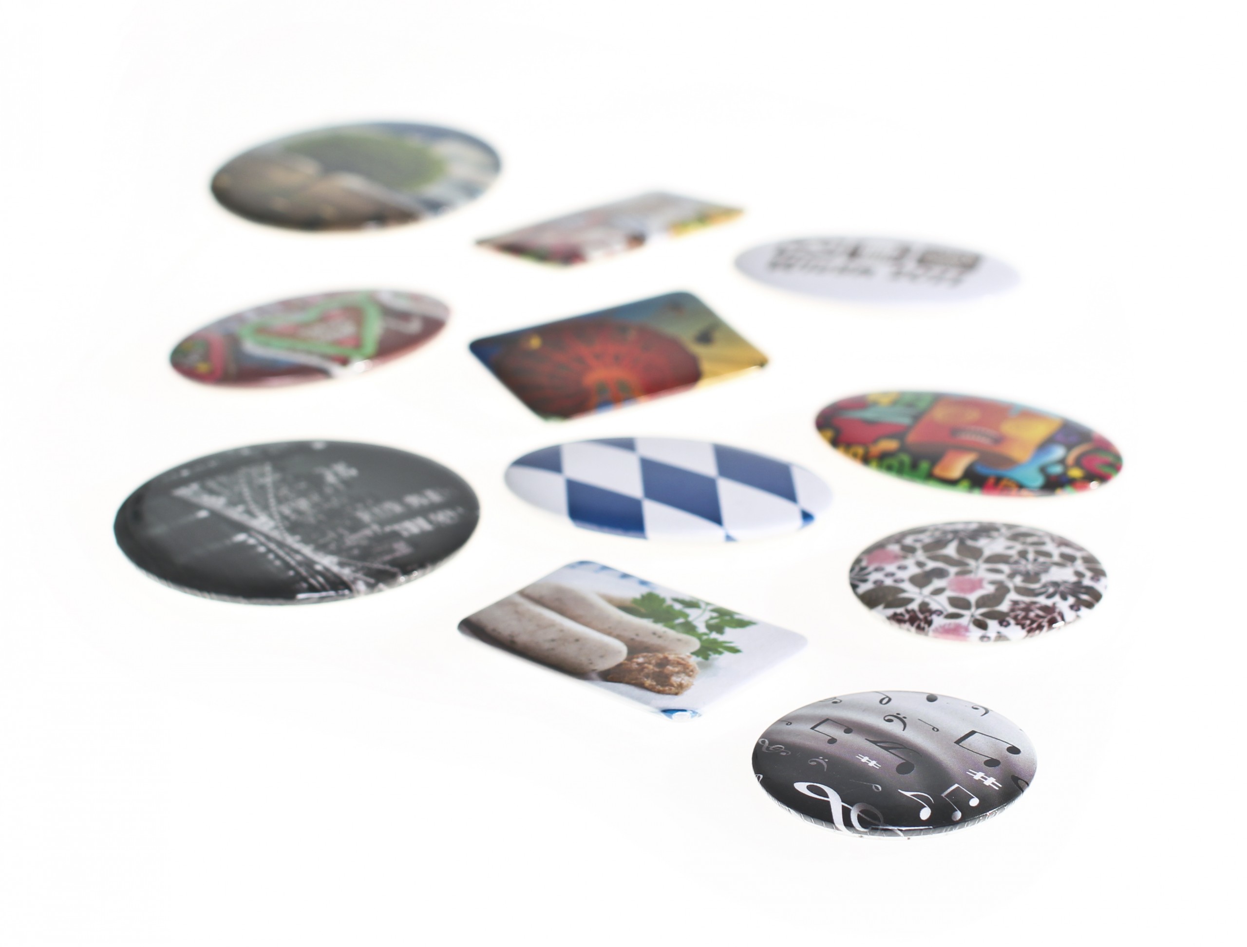 Runde und rechteckige Buttons in verschiedenen Größen mit Motiven wie bayerischer Raute, Weißwürsten, Lebkuchenherz und Musiknoten