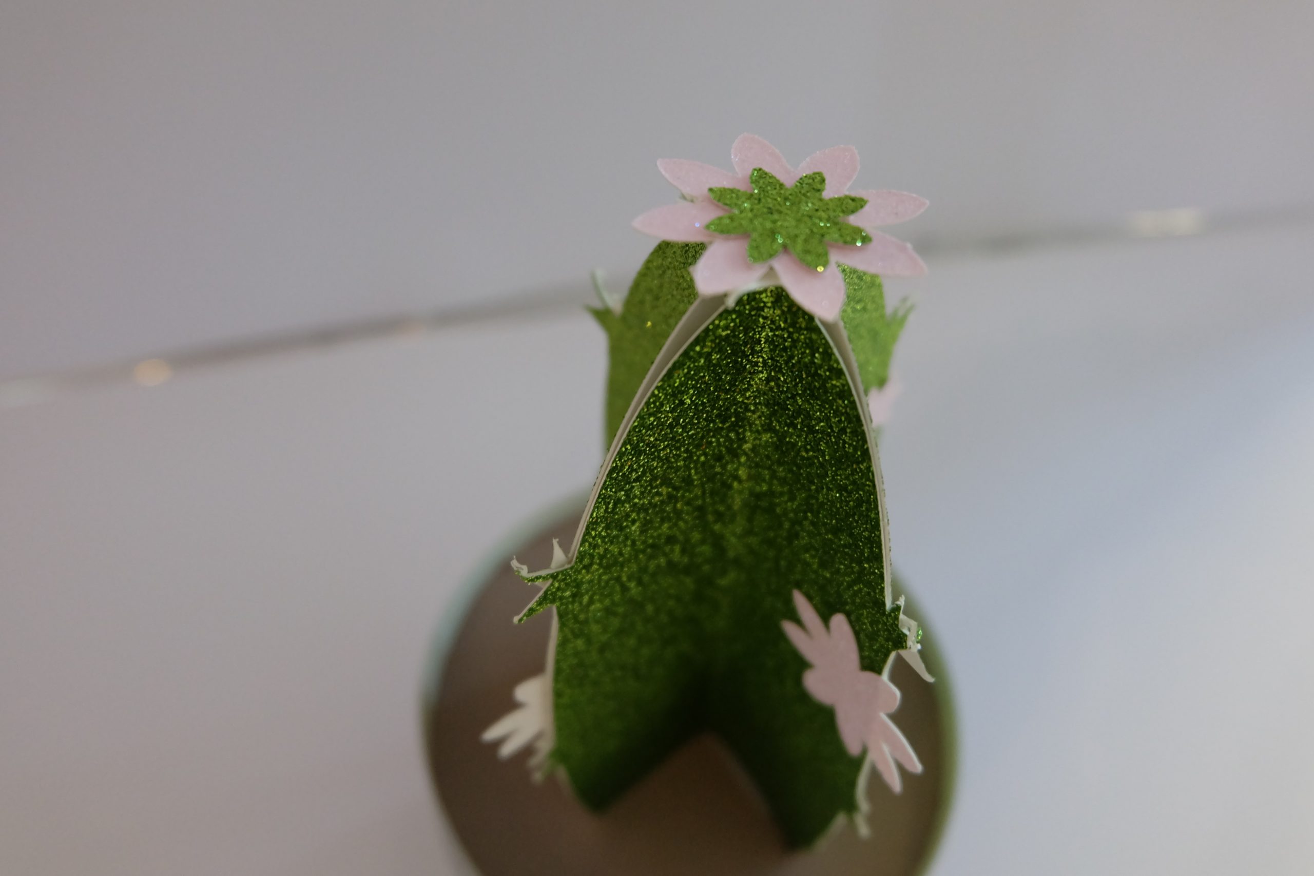 Zusammengeklebter 3D-Kaktus aus grünem Glitzerpapier mit rosa Blüte, auf ausgeplottetem Kreis als Boden befestigt
